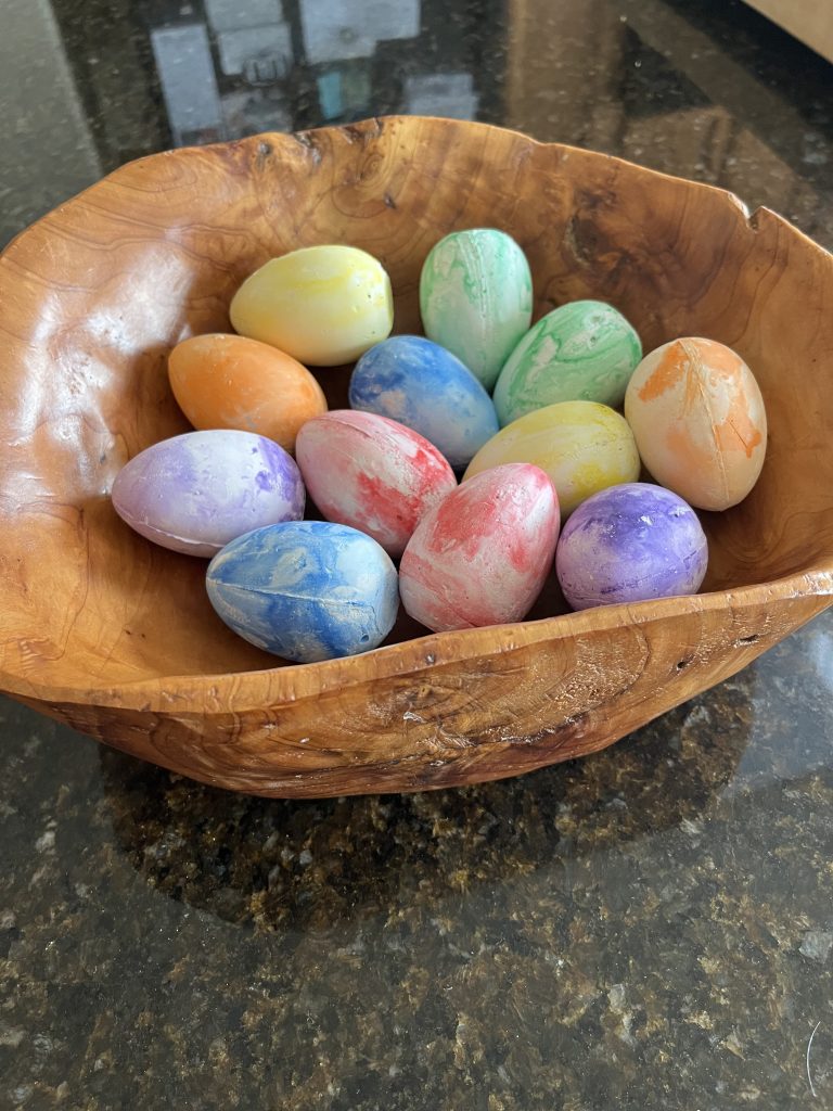 brightly colored chalk eggs in knotty wooden bowl on dark, shiny stone counter