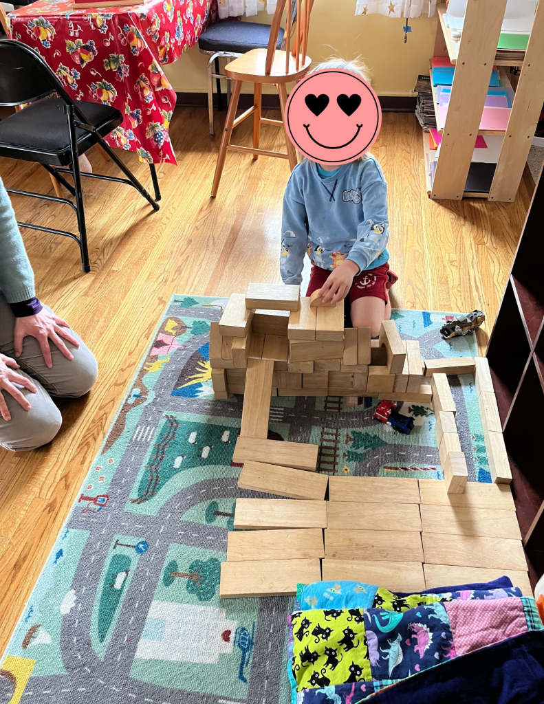 young child building large array of wooden blocks on a rug on the floor
