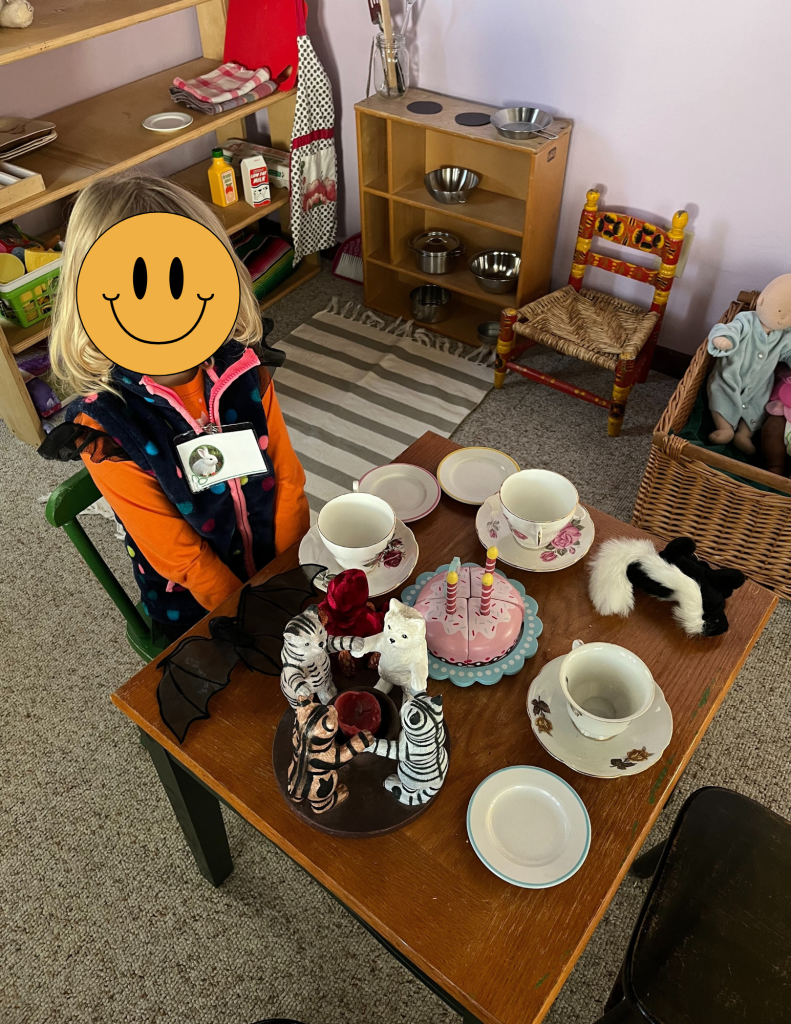 young child sitting at a table with pretend tea cups and teapot