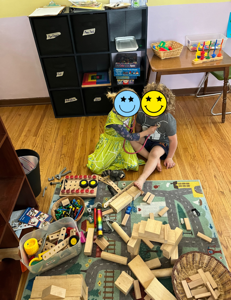 two children sitting by rug covered in wooden train track pieces and building blocks