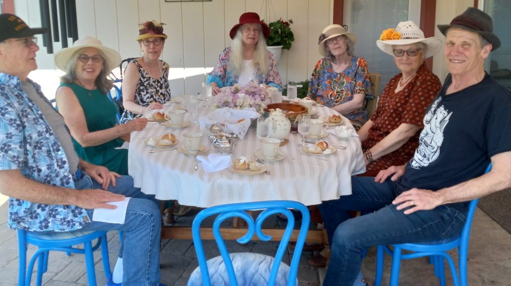 uucm members sit around blue painted patio table with fancy hats at a "high tea" themed circle supper
