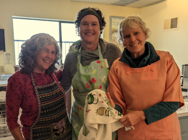 Shannon Dooley-Miller, Laura Harter, and Laurie Bell in UUCM's kitchen, wearing aprons and smocks donated to the Hospitality Volunteers (November 2022)