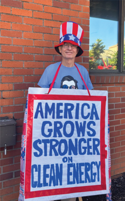 Keith Johnson in an 'Uncle Sam' hat and sandwich board that reads, "America Grows Stronger with Clean Energy" at Fourth of July parade in Nevada City, CA